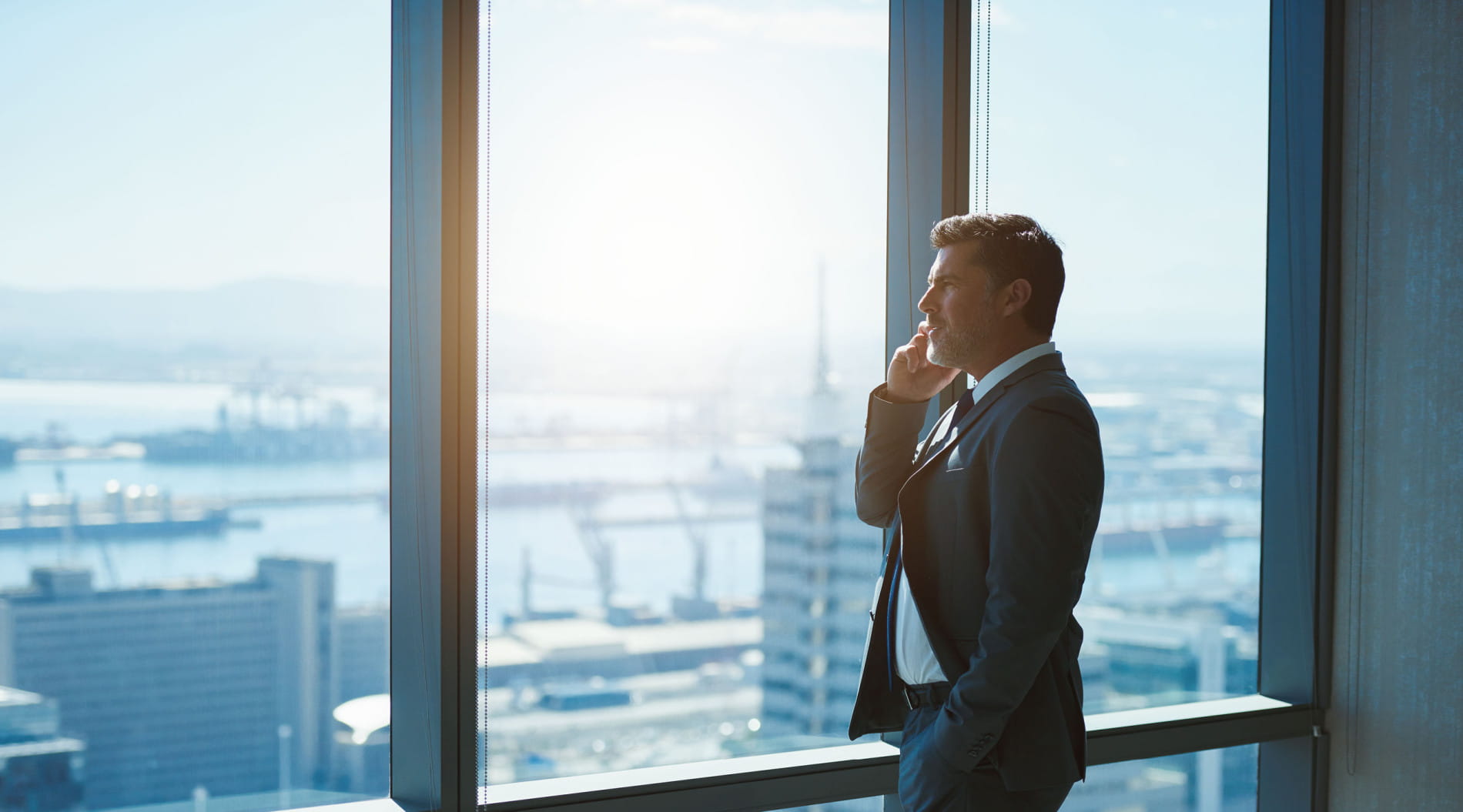 Person on phone by office window overlooking urban landscape Person on phone by office window overlooking urban landscape
