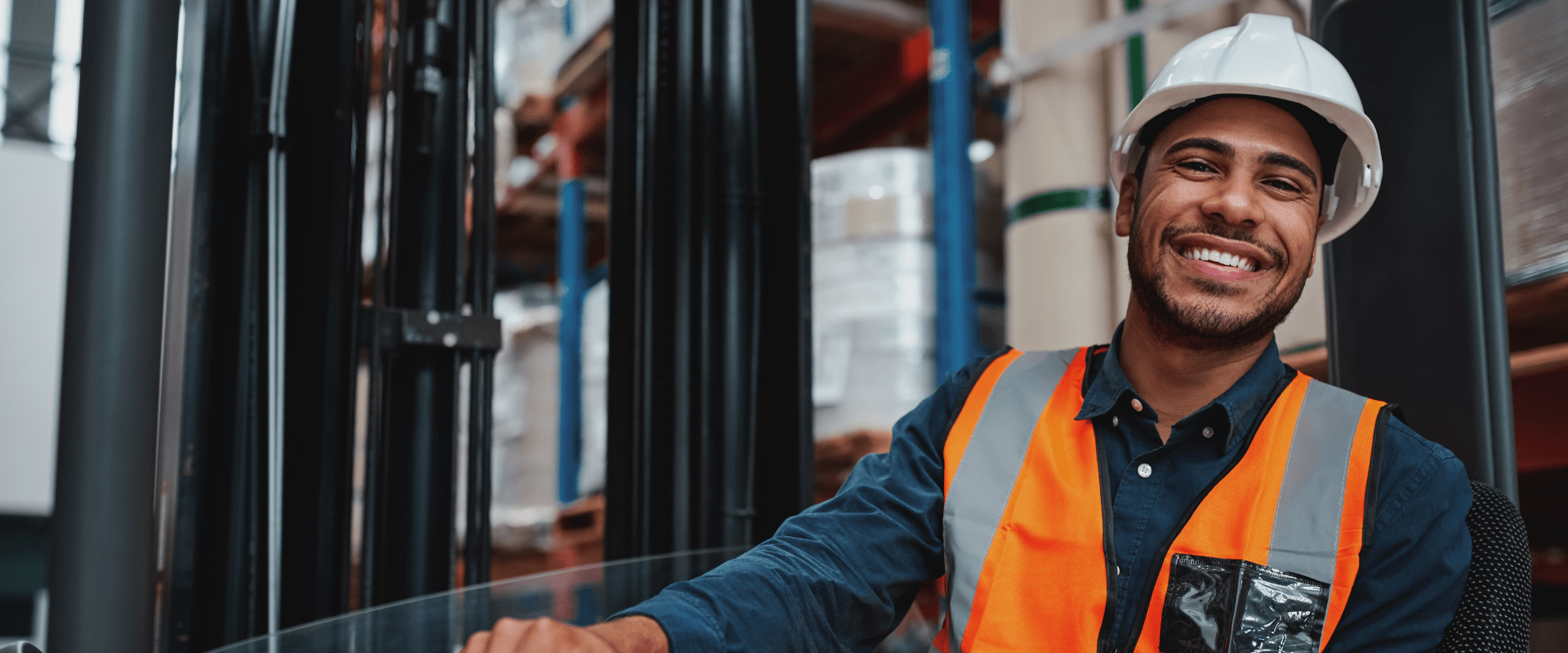 Leende truckförare i skyddsutrustning  arbetar i ett lager.