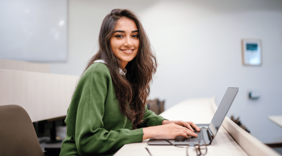 Leende kvinna vid laptop, symboliserande och positivitet och framåtanda.