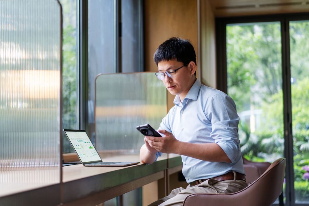 Person using a smartphone while working at a laptop in a modern office. Person using a smartphone while working at a laptop in a modern office.