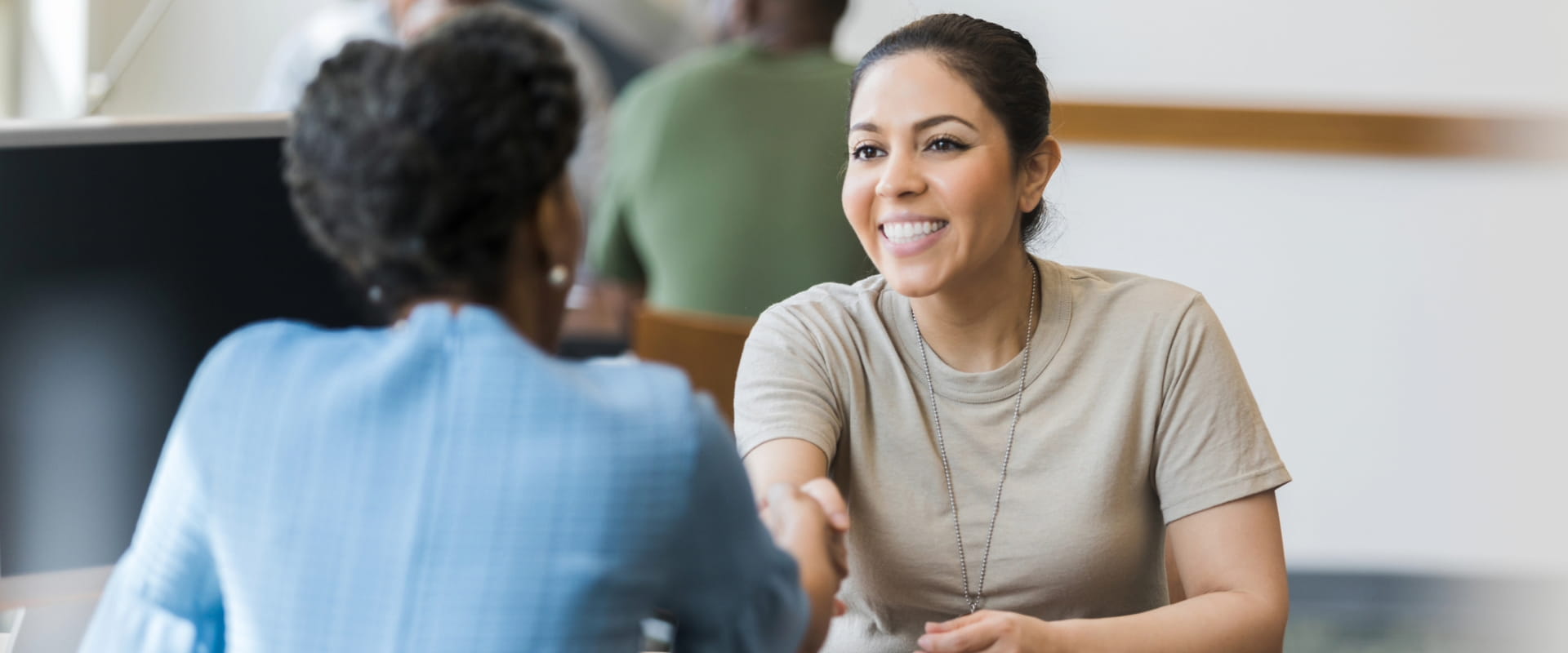 A smiling veteran in partial uniform shakes hands with a hiring manager across the desk.