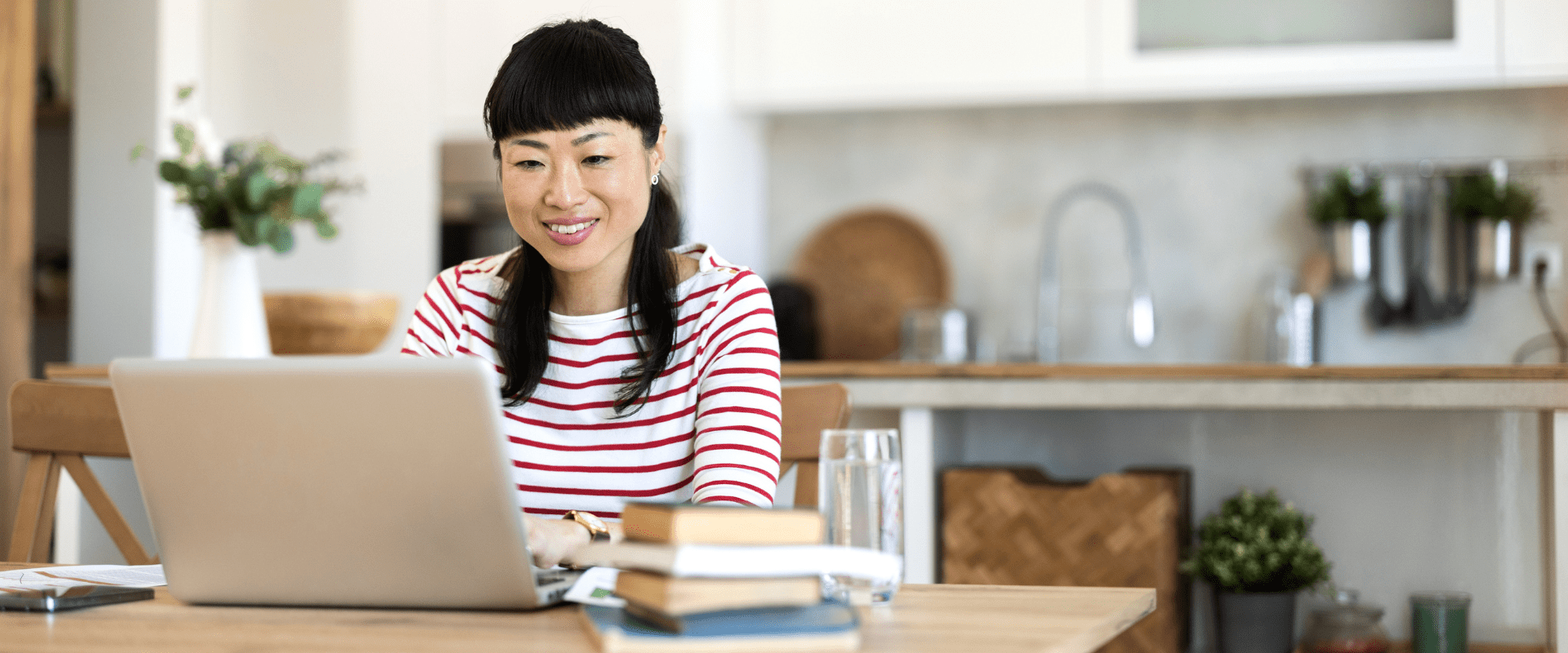 A person sits, writing at their laptop in their kitchen