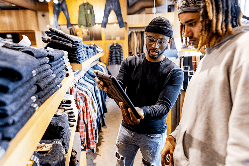 Retail worker helping a customer in a clothing store using a tablet, demonstrating customer service skills and entry-level retail job experience.