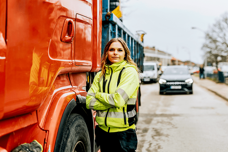 Female truck driver and logistics professional standing next to a commercial vehicle in high-visibility workwear, highlighting careers in transport and logistics.