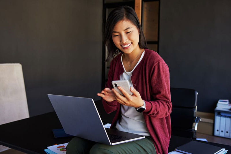 Professional using a smartphone and laptop to review work and employee benefits.