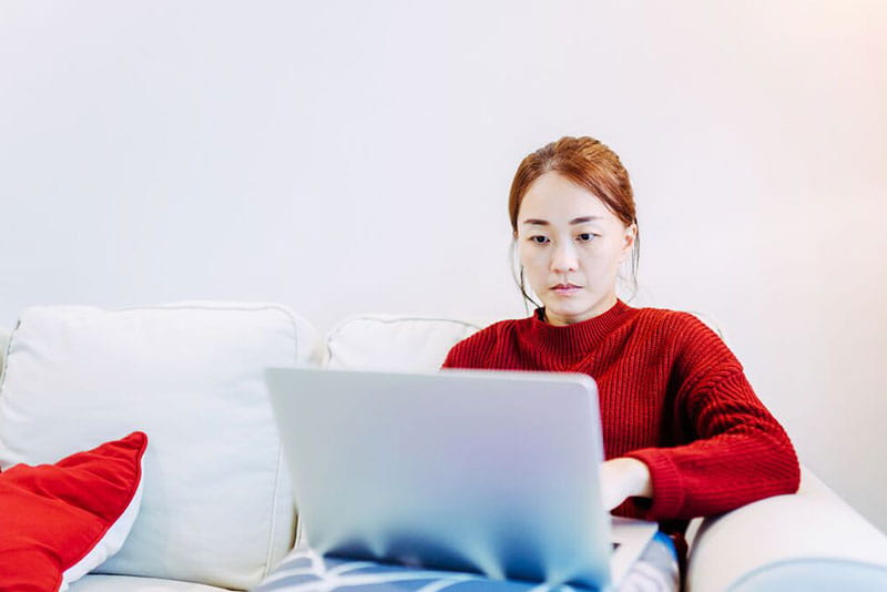 Person sitting on a sofa using a laptop at home, preparing or participating in a video interview.