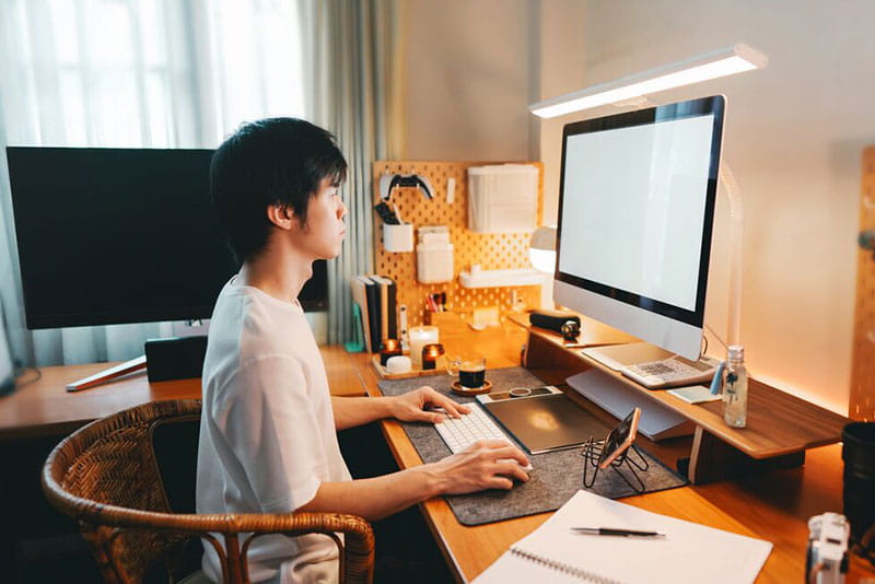 Person working at a desktop computer in a home office with a well-organised workspace and dual monitors.