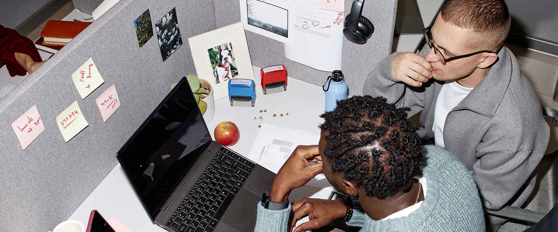 Two colleagues collaborating at a desk with a laptop in a creative workspace