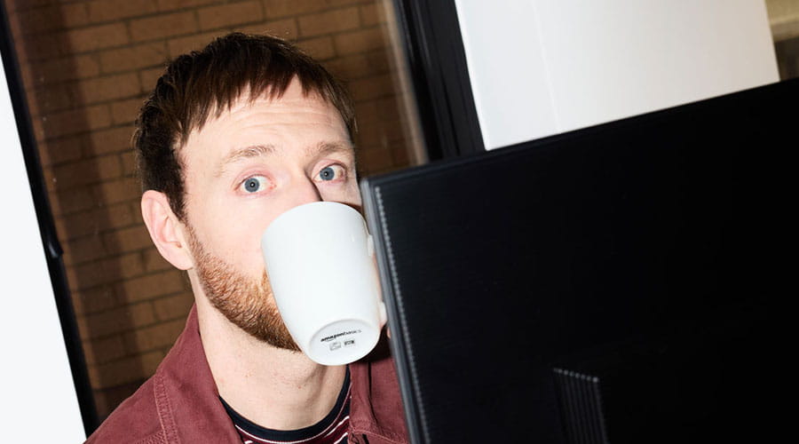Man dricker kaffe medan han arbetar vid dator
