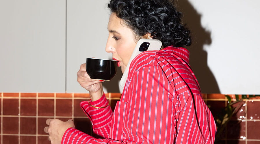 Kvinna dricker kaffe och talar i telefon i kök Kvinna dricker kaffe och talar i telefon i kök