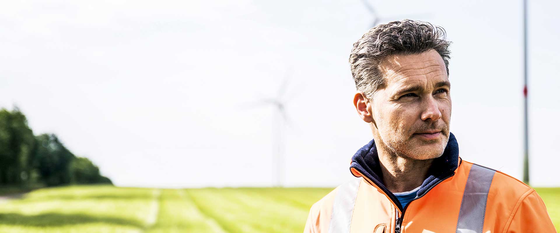 Wind energy technician standing in field near turbines