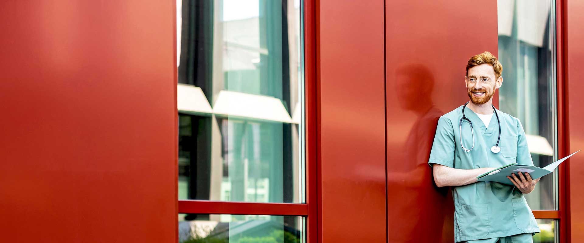 Infirmier debout avec une tablette contre un mur rouge à l'extérieur
