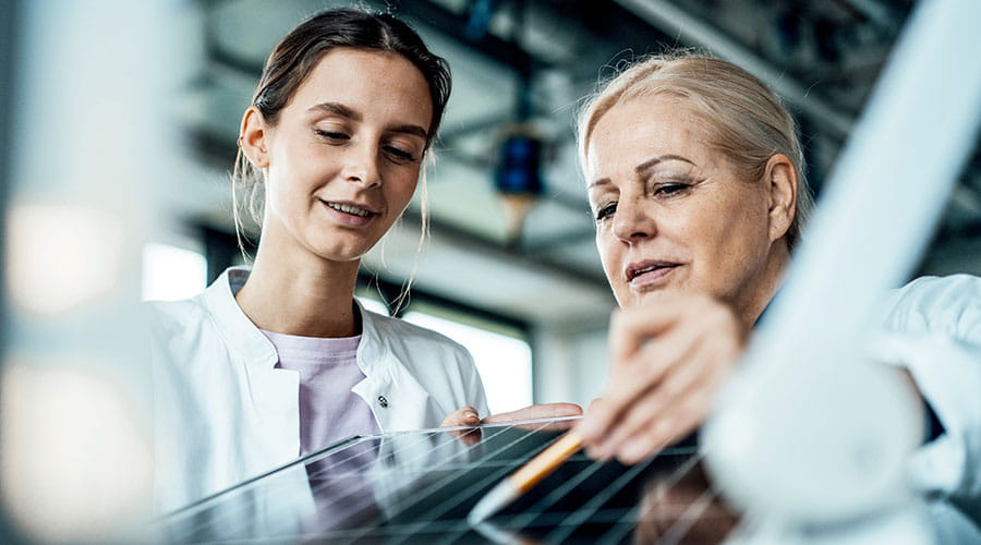 Deux femmes en blouse regardent et discutent autour d’un écran tactile dans un laboratoire