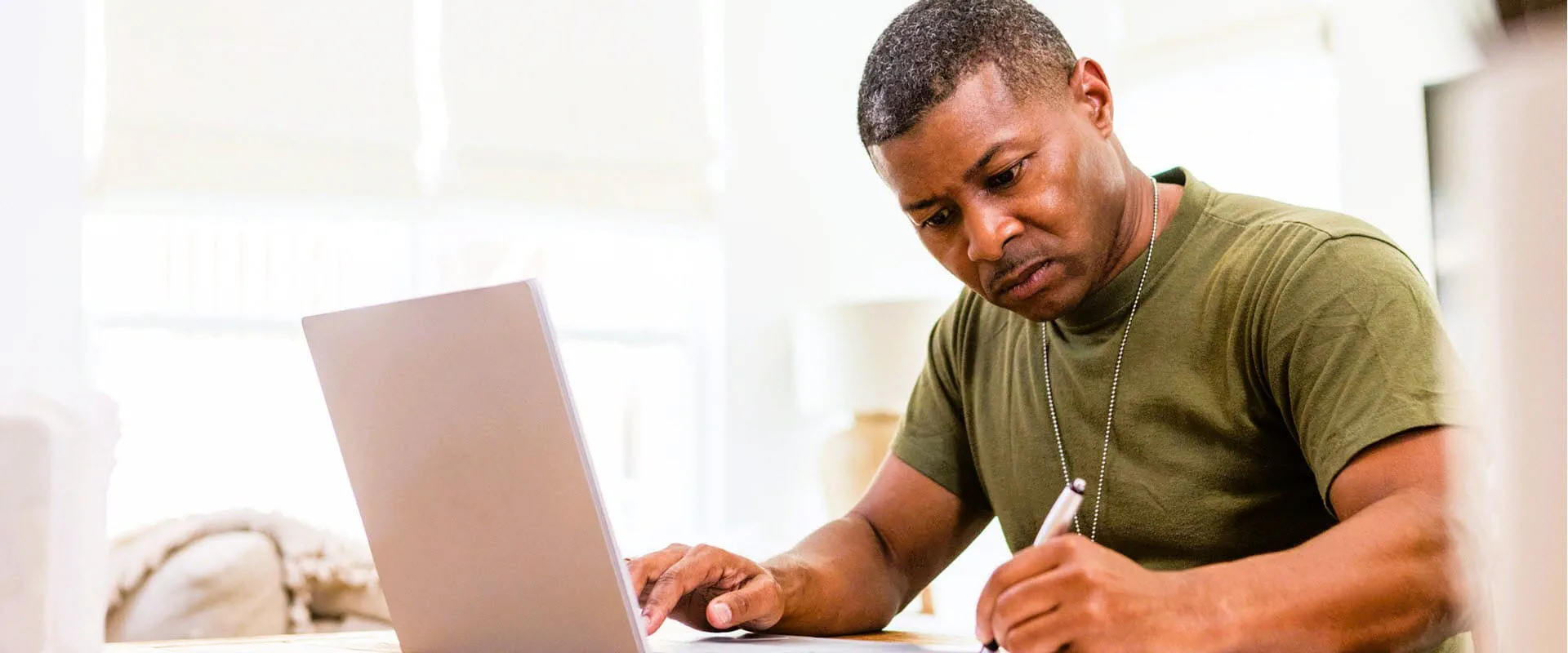 Focused man working on a laptop and writing notes at a table Focused man working on a laptop and writing notes at a table