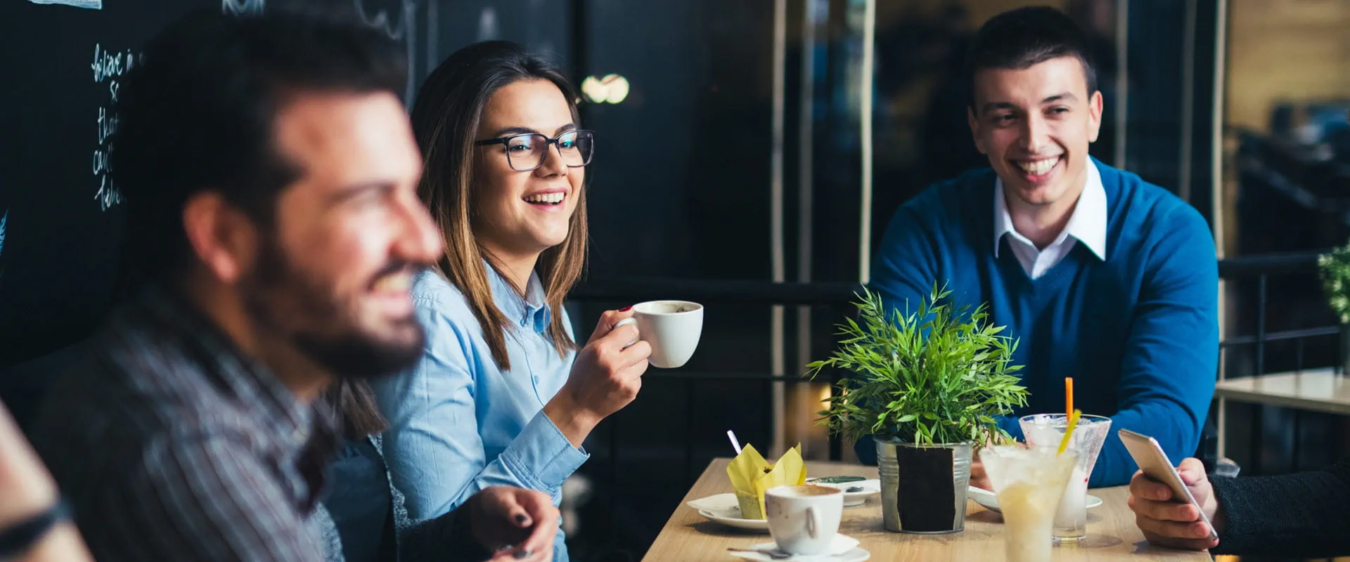 A group of young people sit around a table drinking coffee at a restaurant. A group of young people sit around a table drinking coffee at a restaurant.
