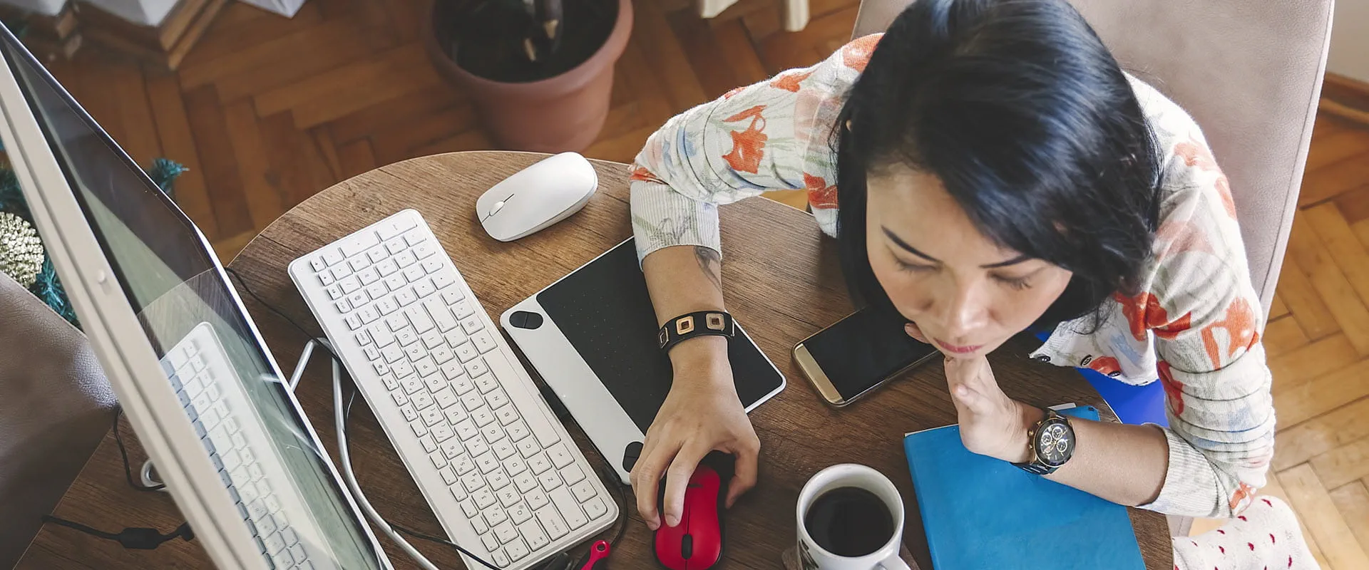 An individual sits at their desk with a desktop computer, laptop, phone, notebook, and cup of coffee, during their job search. An individual sits at their desk with a desktop computer, laptop, phone, notebook, and cup of coffee, during their job search.