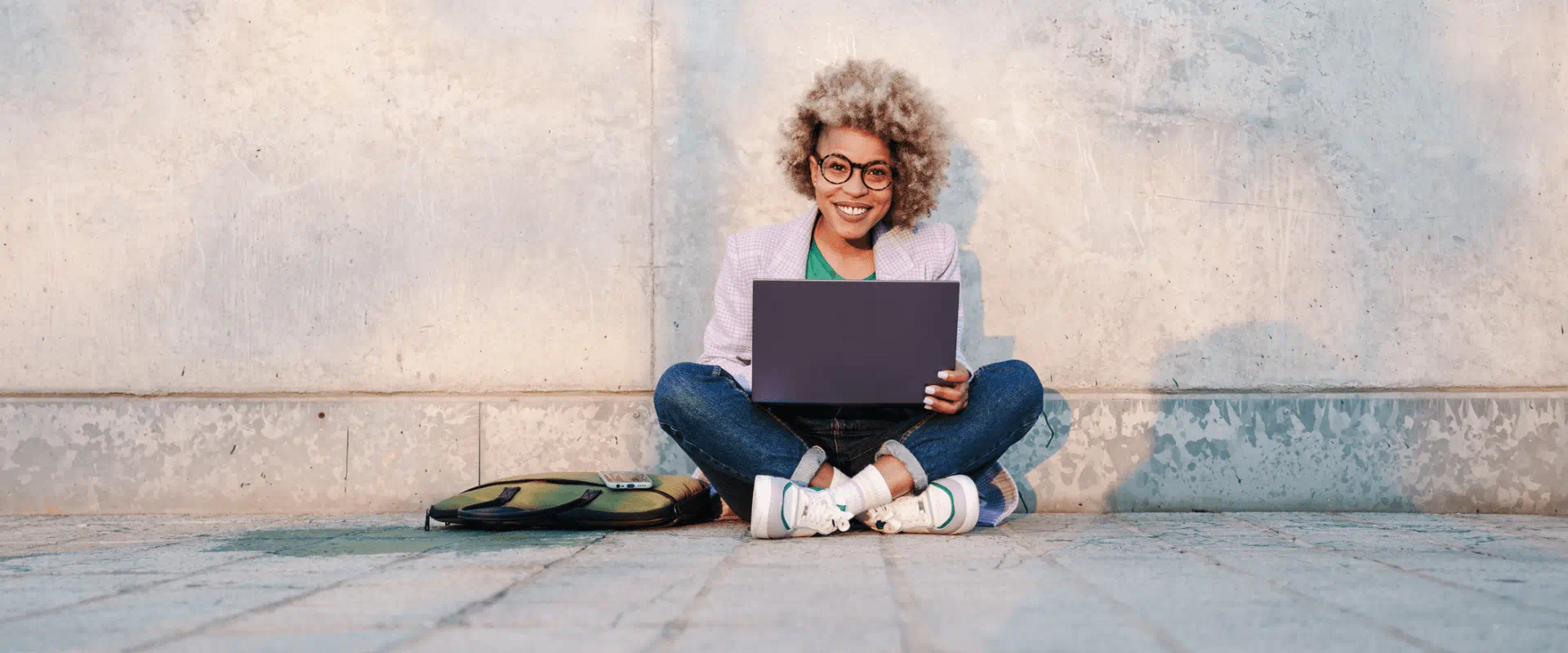 A smiling person sits outside with a laptop in their lap. A smiling person sits outside with a laptop in their lap.