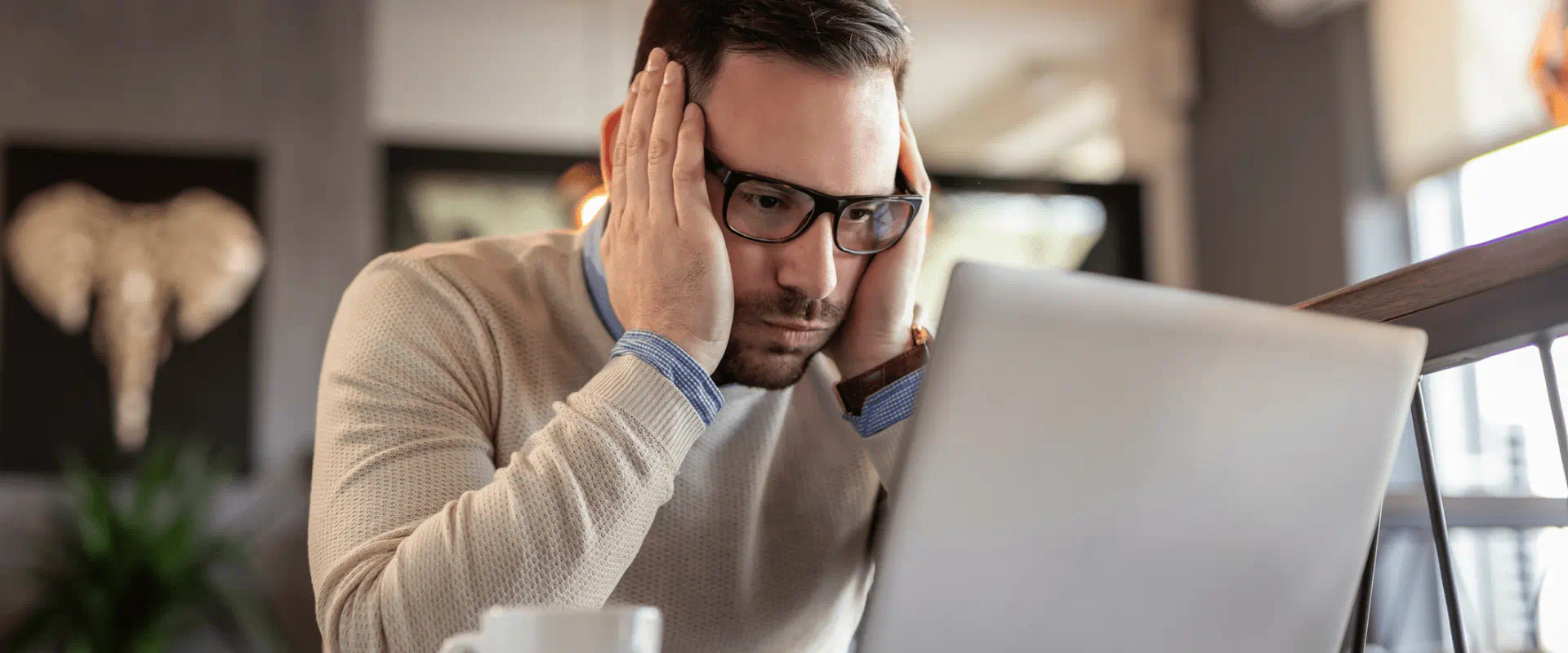 A person looks at their laptop in a coffee shop, seemingly frustrated. A person looks at their laptop in a coffee shop, seemingly frustrated.