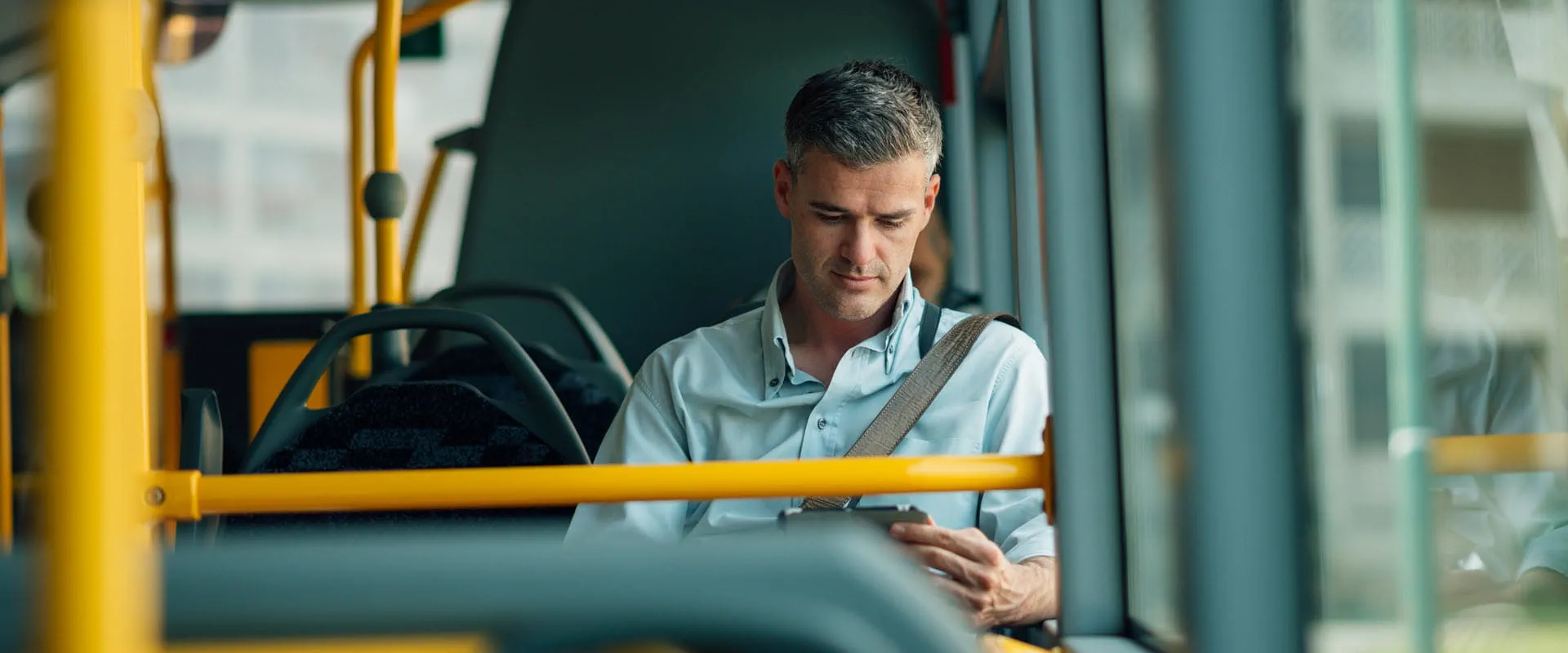 A person sitting alone on a bus, looking at their smartphone with a focused expression. A person sitting alone on a bus, looking at their smartphone with a focused expression.