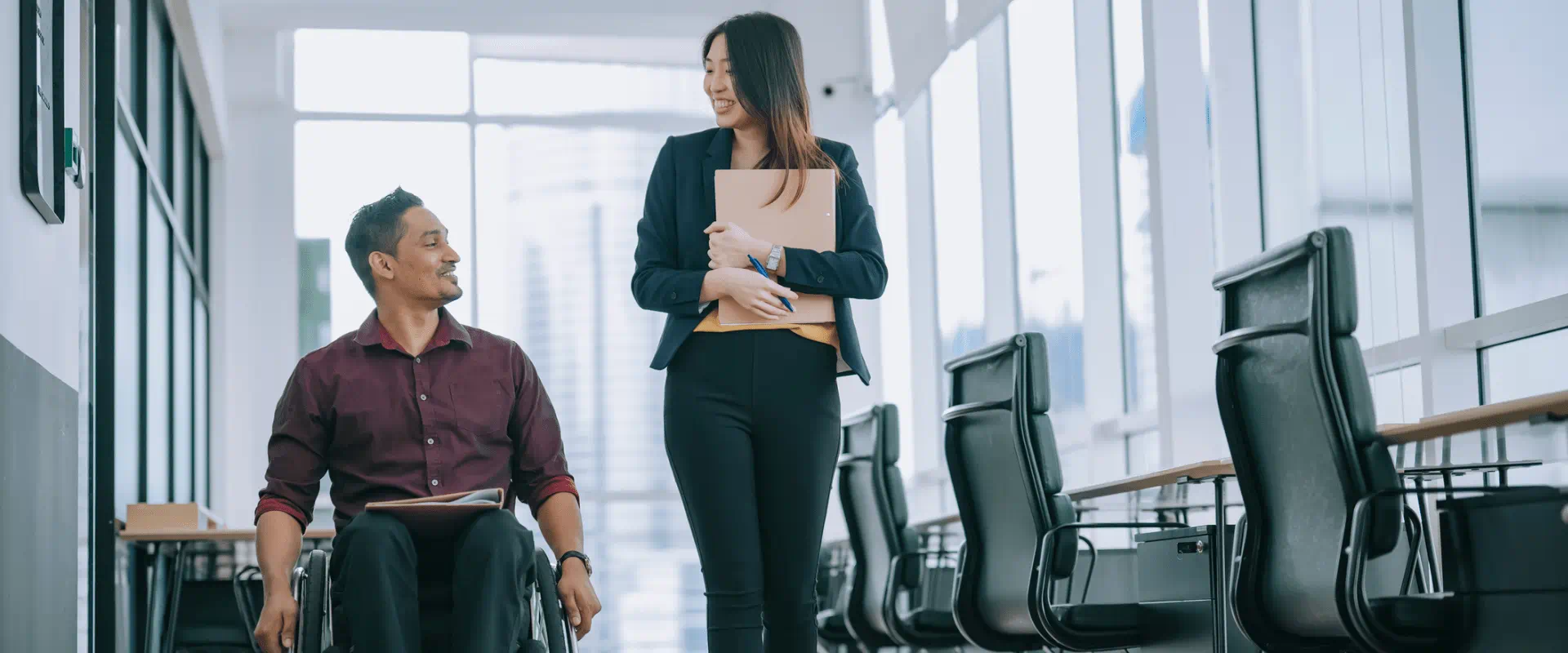Two workers, one walking and the other in a wheelchair, head down an office hallway.
