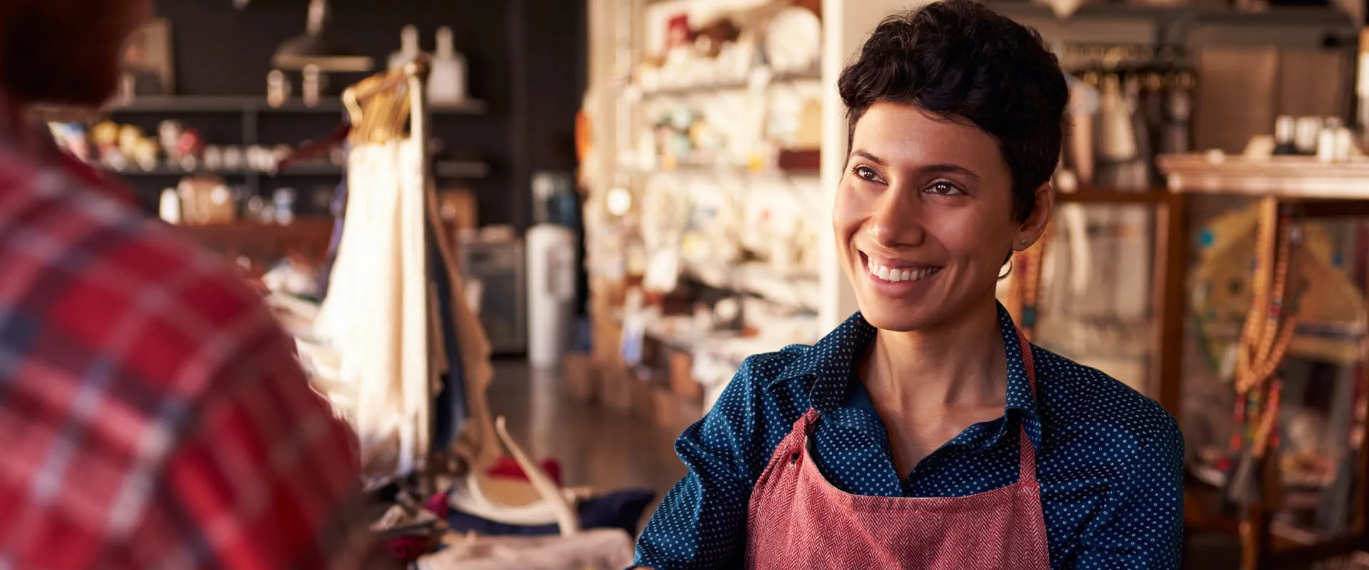 A smiling retail worker wearing an apron assists a customer at a boutique store.