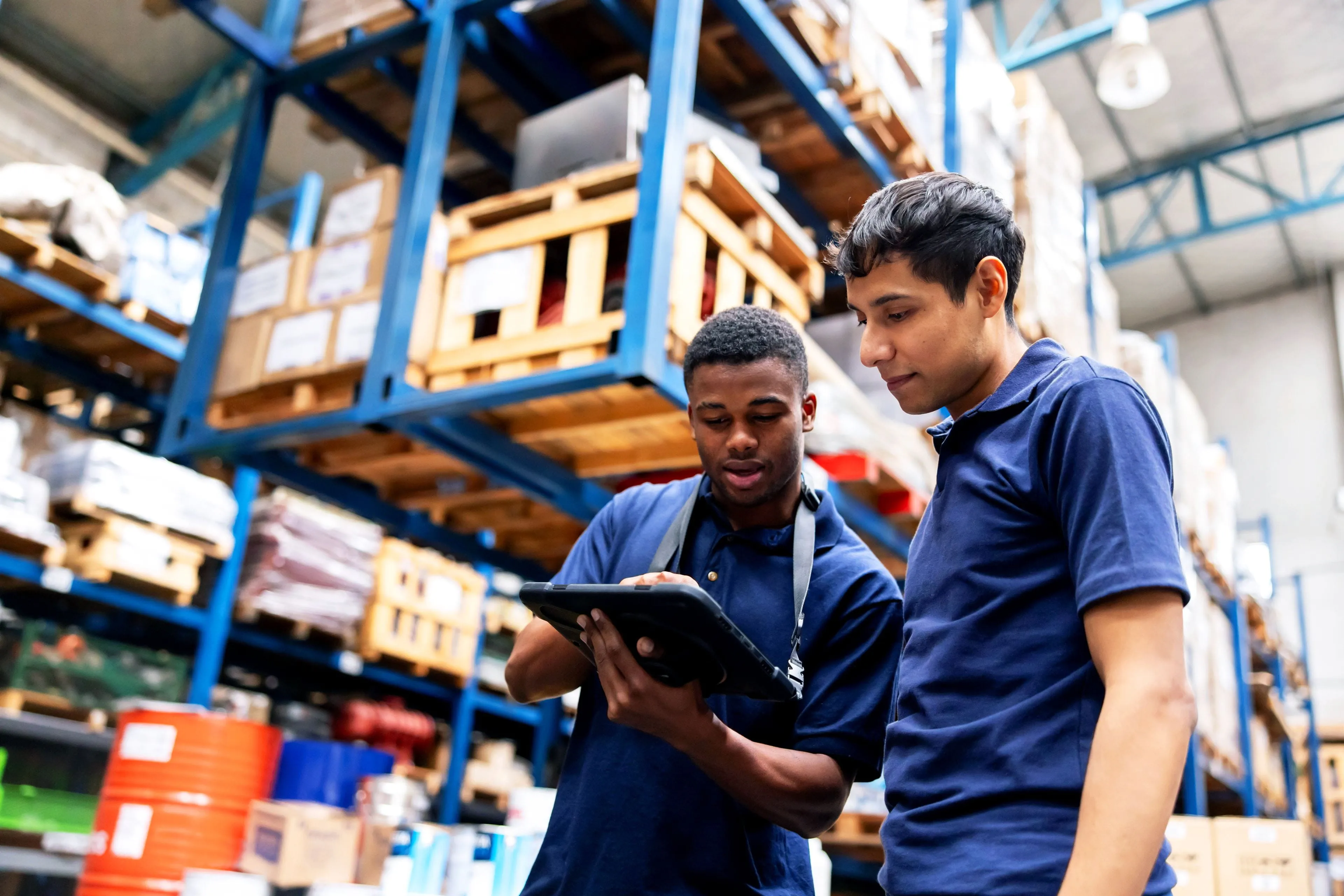 Two warehouse workers review inventory on a tablet in a distribution center Two warehouse workers review inventory on a tablet in a distribution center