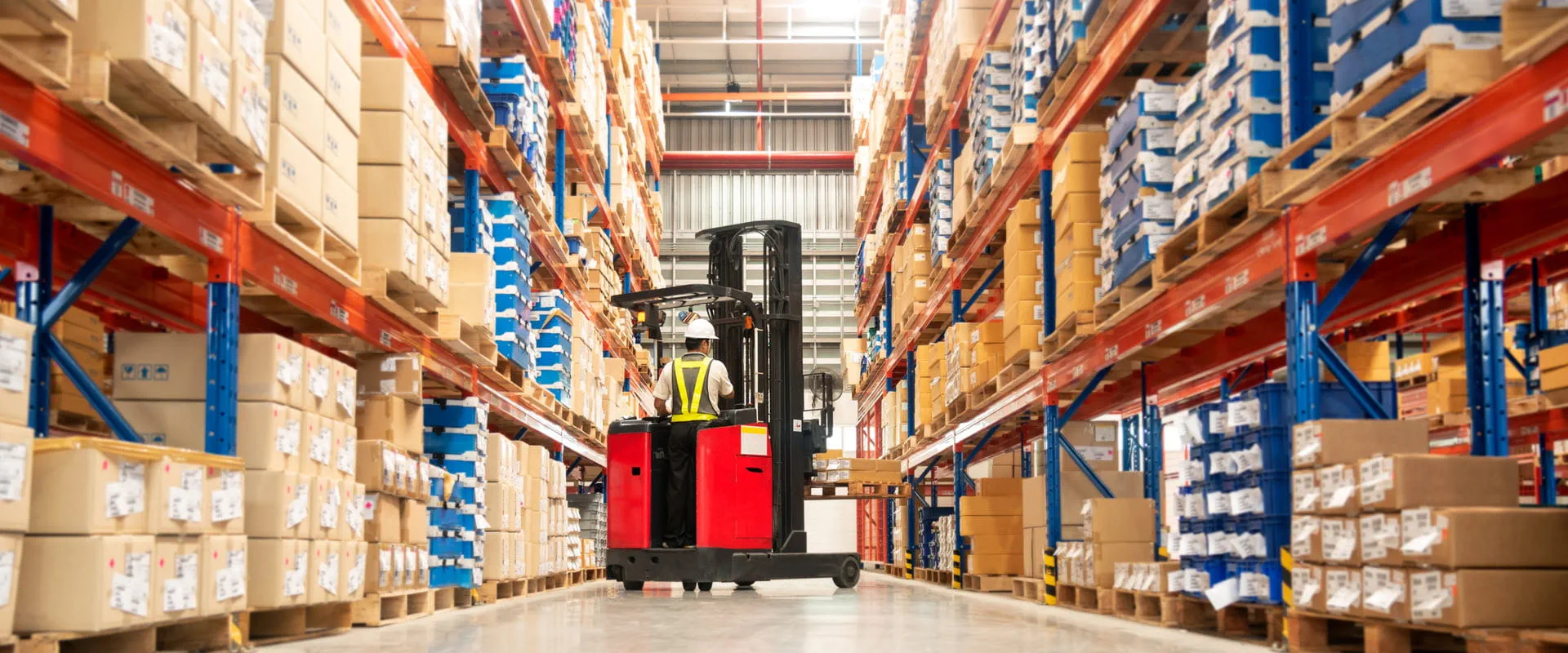 Worker in forklift-truck loading packed goods in huge distribution warehouse with high shelves. Worker in forklift-truck loading packed goods in huge distribution warehouse with high shelves.