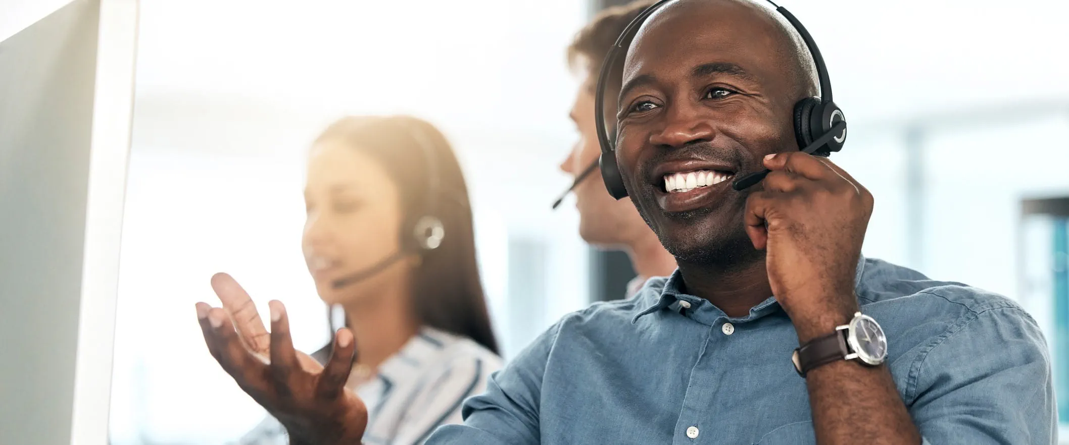 A call center smiles and talks, while wearing a headset. Other call center workers are behind them. A call center smiles and talks, while wearing a headset. Other call center workers are behind them.