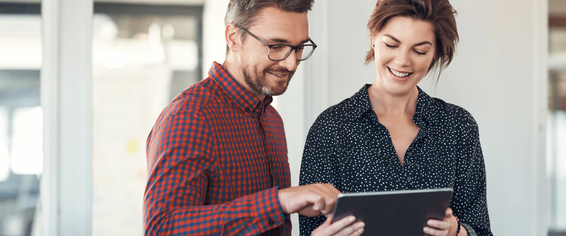 Two people stand next to each other looking at a tablet Two people stand next to each other looking at a tablet