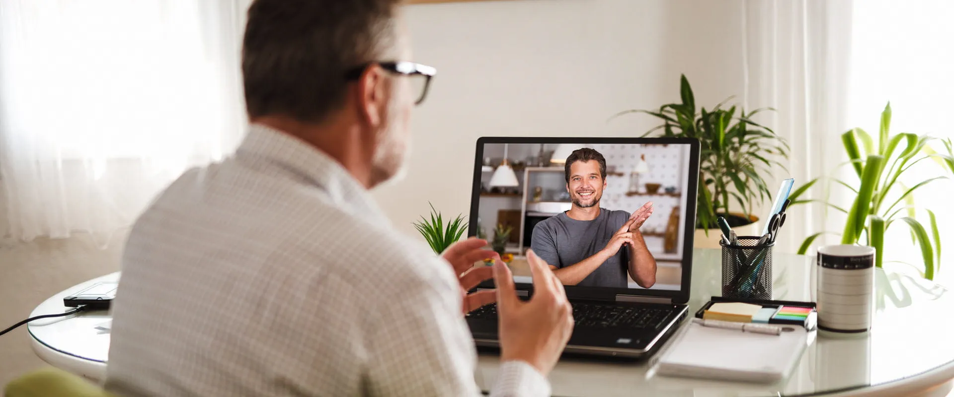 An individual with glasses signs with another person, via video chat, on their laptop. An individual with glasses signs with another person, via video chat, on their laptop.