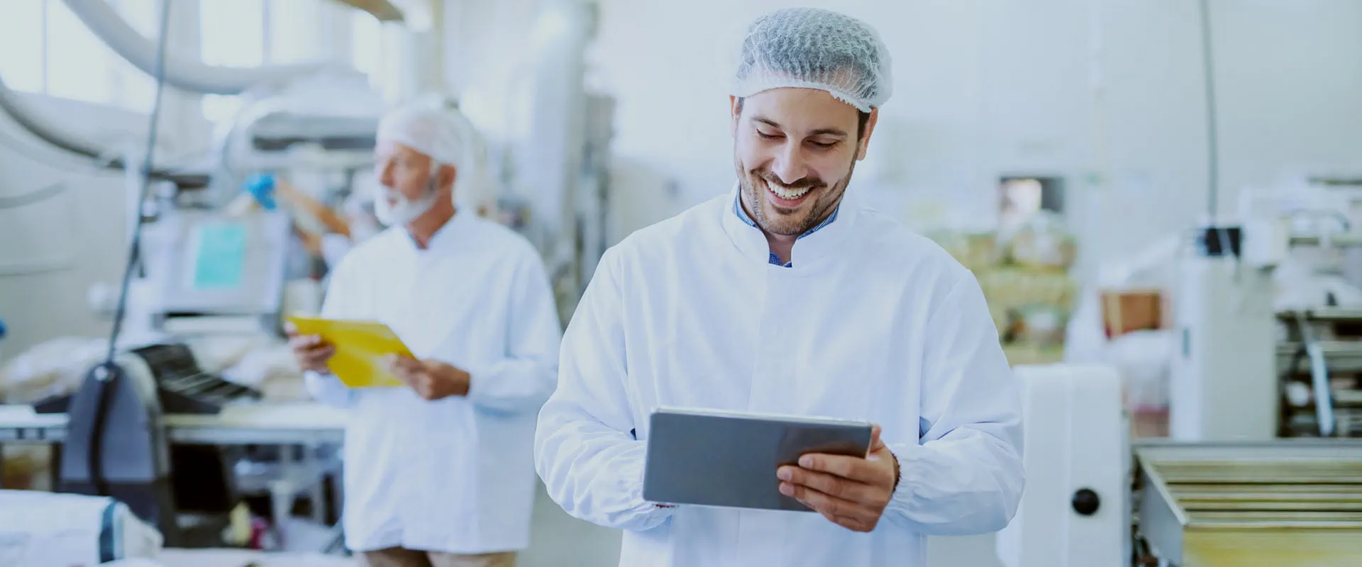 Smiling supervisor in sterile white uniform using tablet while standing in food plant. Smiling supervisor in sterile white uniform using tablet while standing in food plant.