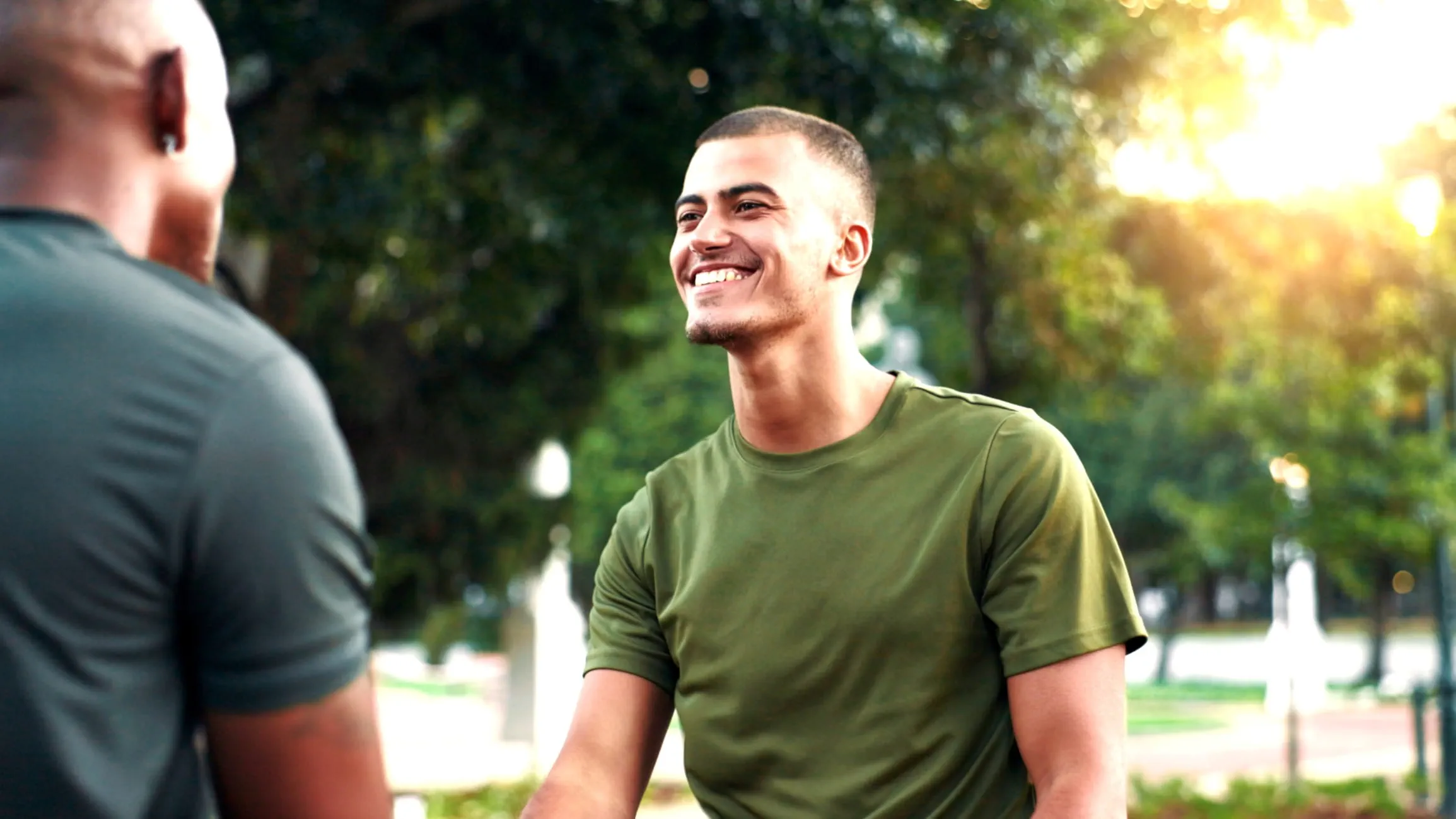 Two people talking outdoors in a park with trees and sunlight in the background. Two people talking outdoors in a park with trees and sunlight in the background.