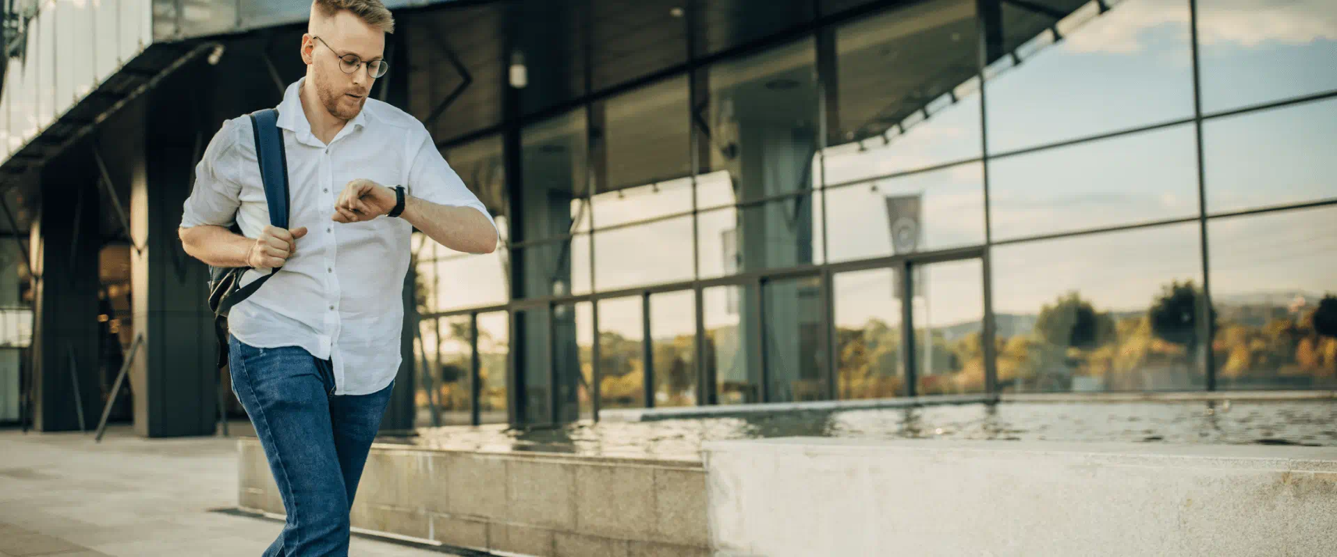 A person in jeans and a button-up shirt jogs outside a building, while looking at their watch A person in jeans and a button-up shirt jogs outside a building, while looking at their watch