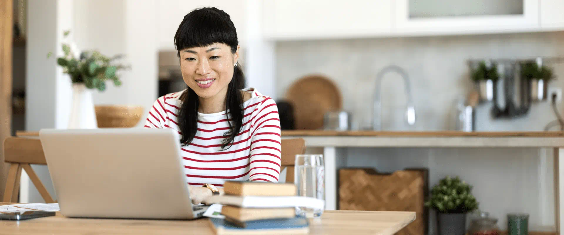 A person sits, writing at their laptop in their kitchen A person sits, writing at their laptop in their kitchen