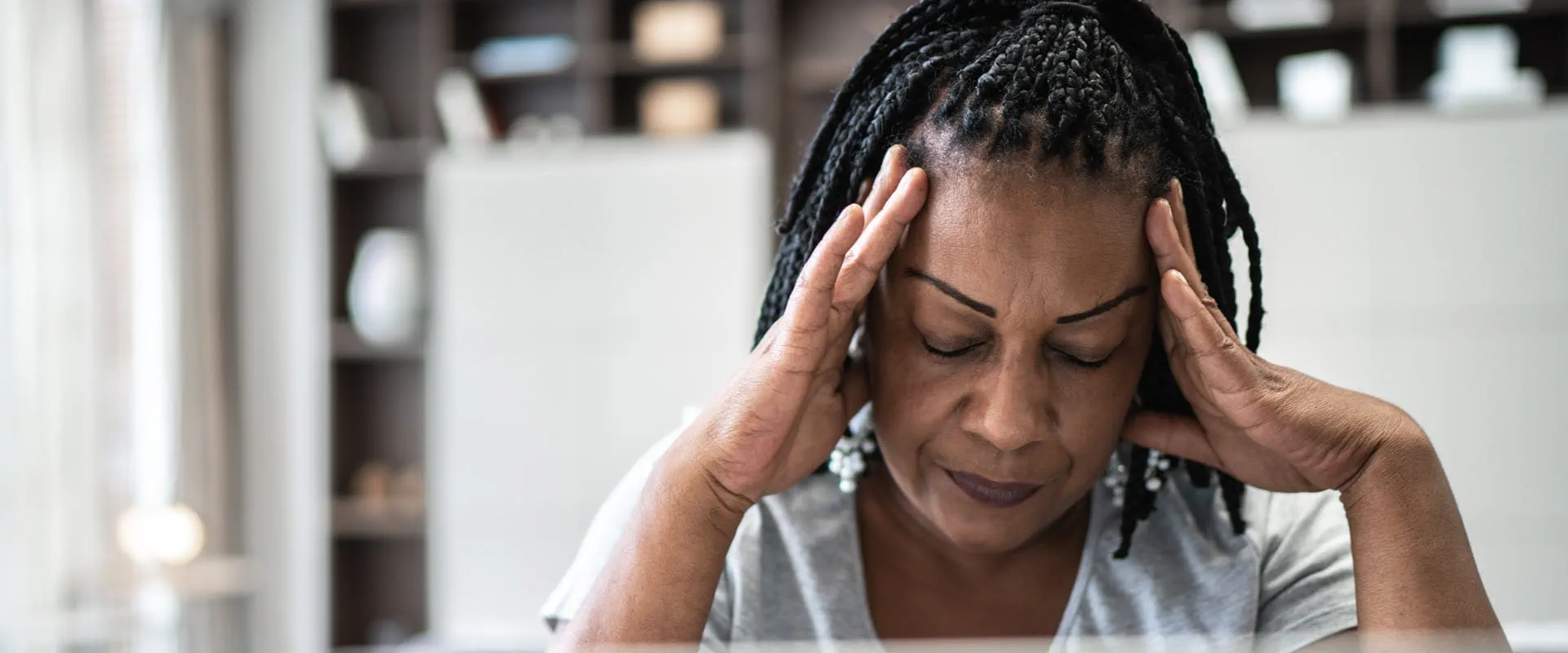 A middle-aged woman sits at home in front of her laptop. Her head is in her hands, seeming stressed. A middle-aged woman sits at home in front of her laptop. Her head is in her hands, seeming stressed.