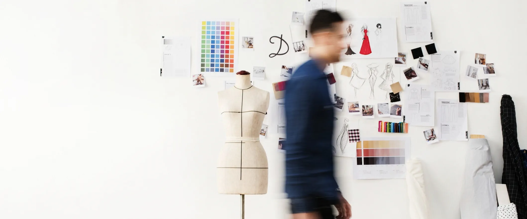 A blurry figure walks past a wall covered in sketches and color swatches.