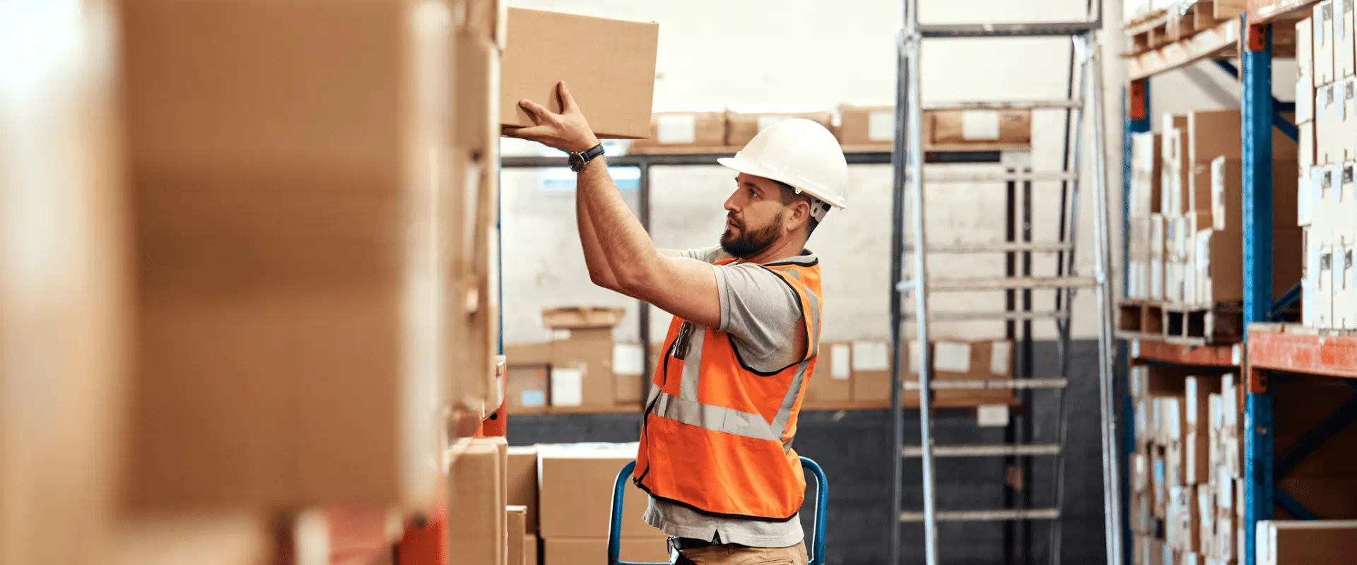 A worker in a warehouse places a box on a high shelf A worker in a warehouse places a box on a high shelf