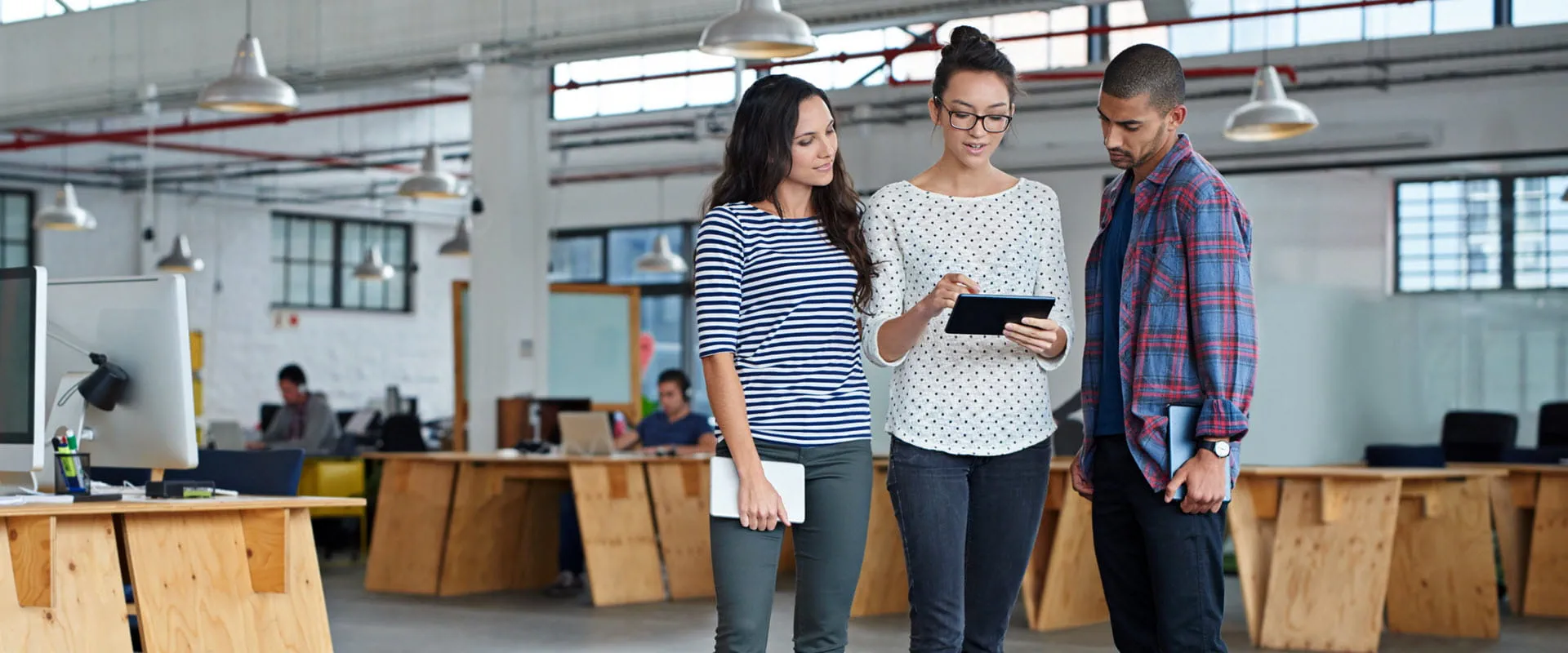Three casually dressed individuals look at a tablet in a modern office space