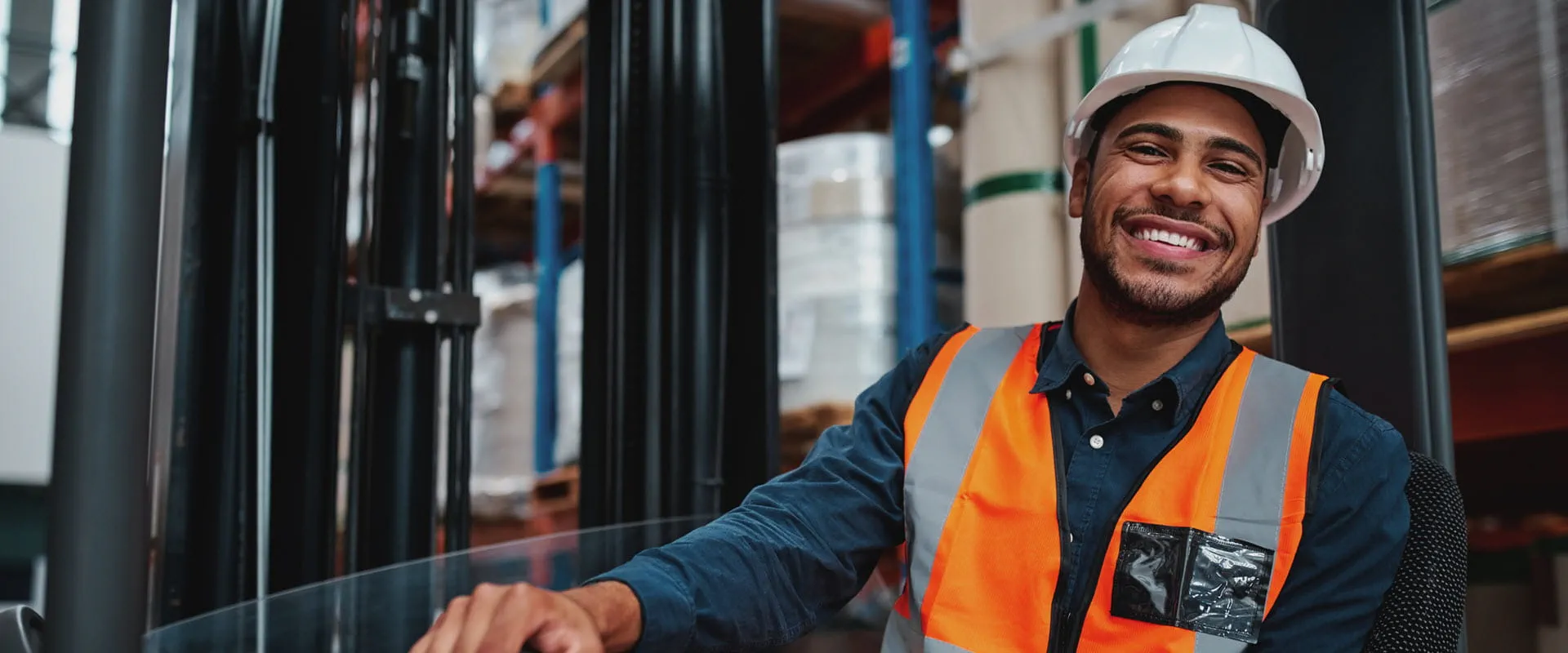 A smiling warehouse worker wearing a white hard hat, high-visibility orange safety vest. A smiling warehouse worker wearing a white hard hat, high-visibility orange safety vest.