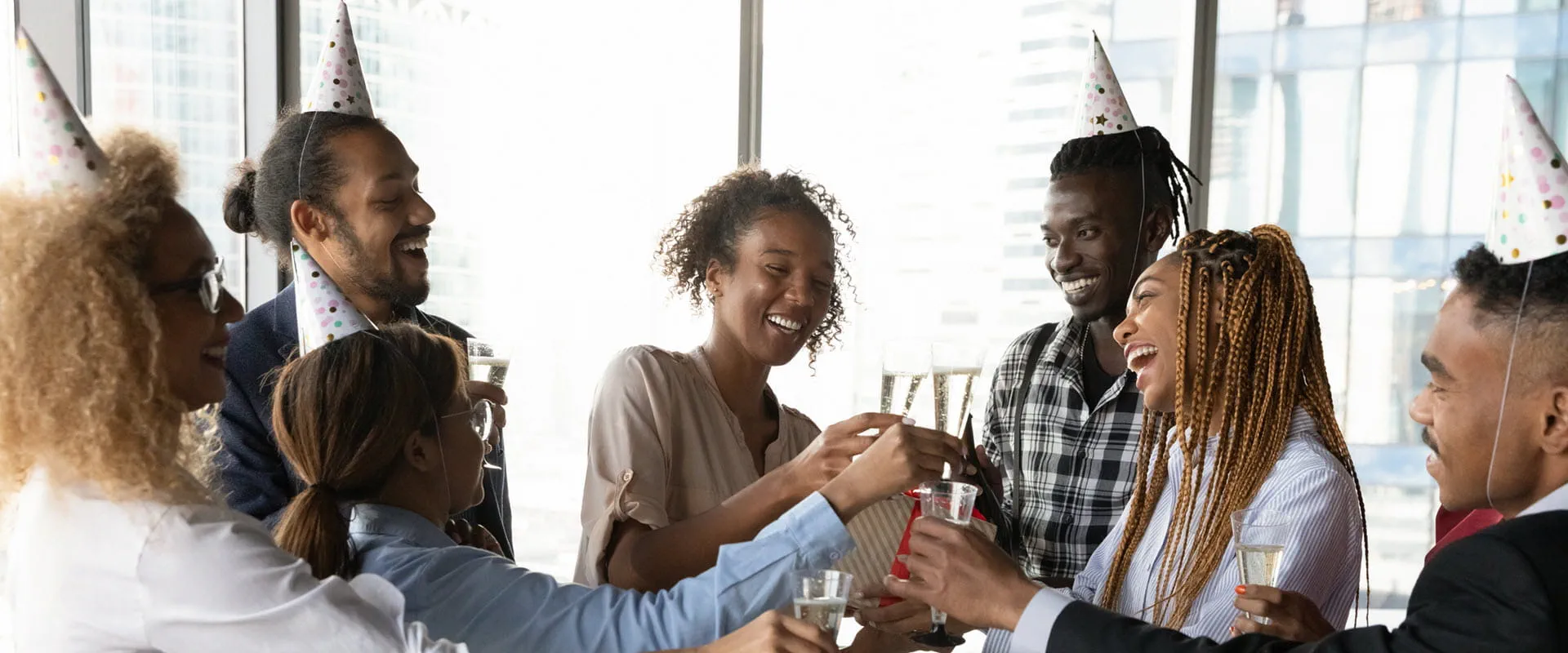 A diverse group of coworkers wearing party hats toast with drinks during an office celebration. A diverse group of coworkers wearing party hats toast with drinks during an office celebration.