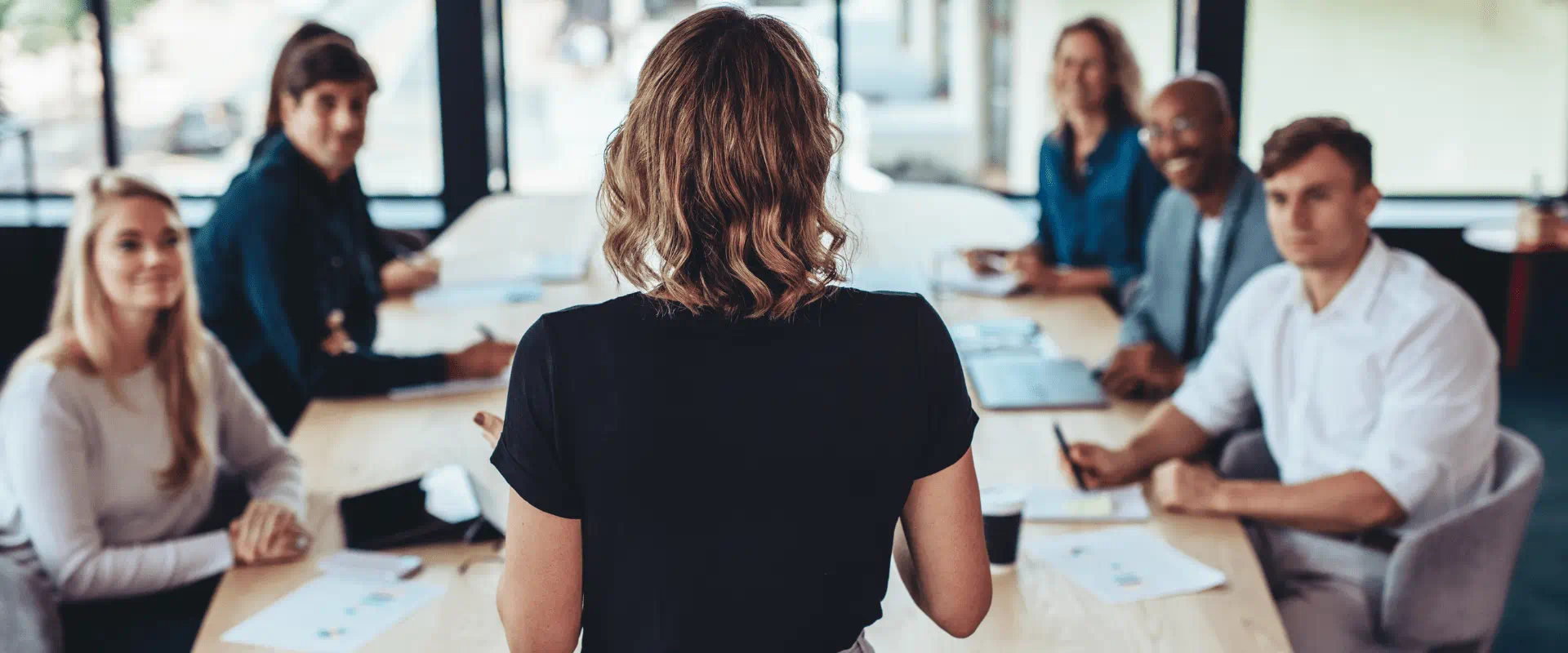 A group of people sit at a conference table looking up at someone who is speaking. A group of people sit at a conference table looking up at someone who is speaking.