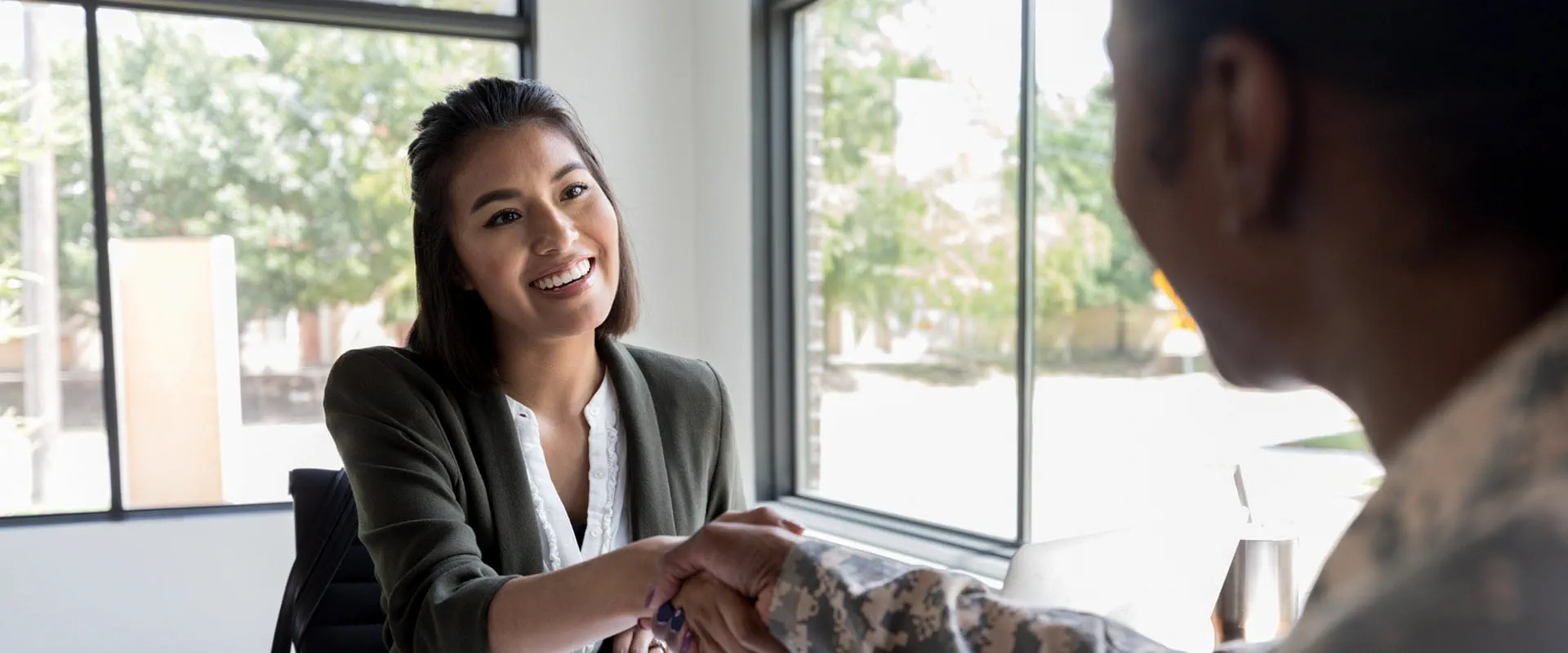 A smiling hiring manager shakes a veteran in uniforms hand across a desk. A smiling hiring manager shakes a veteran in uniforms hand across a desk.