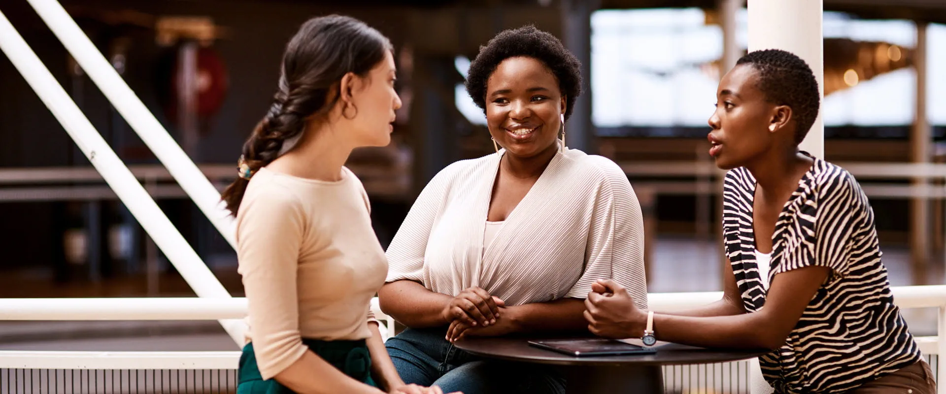 Three diverse individuals engaged in a friendly conversation at a modern office or coworking space. Three diverse individuals engaged in a friendly conversation at a modern office or coworking space.