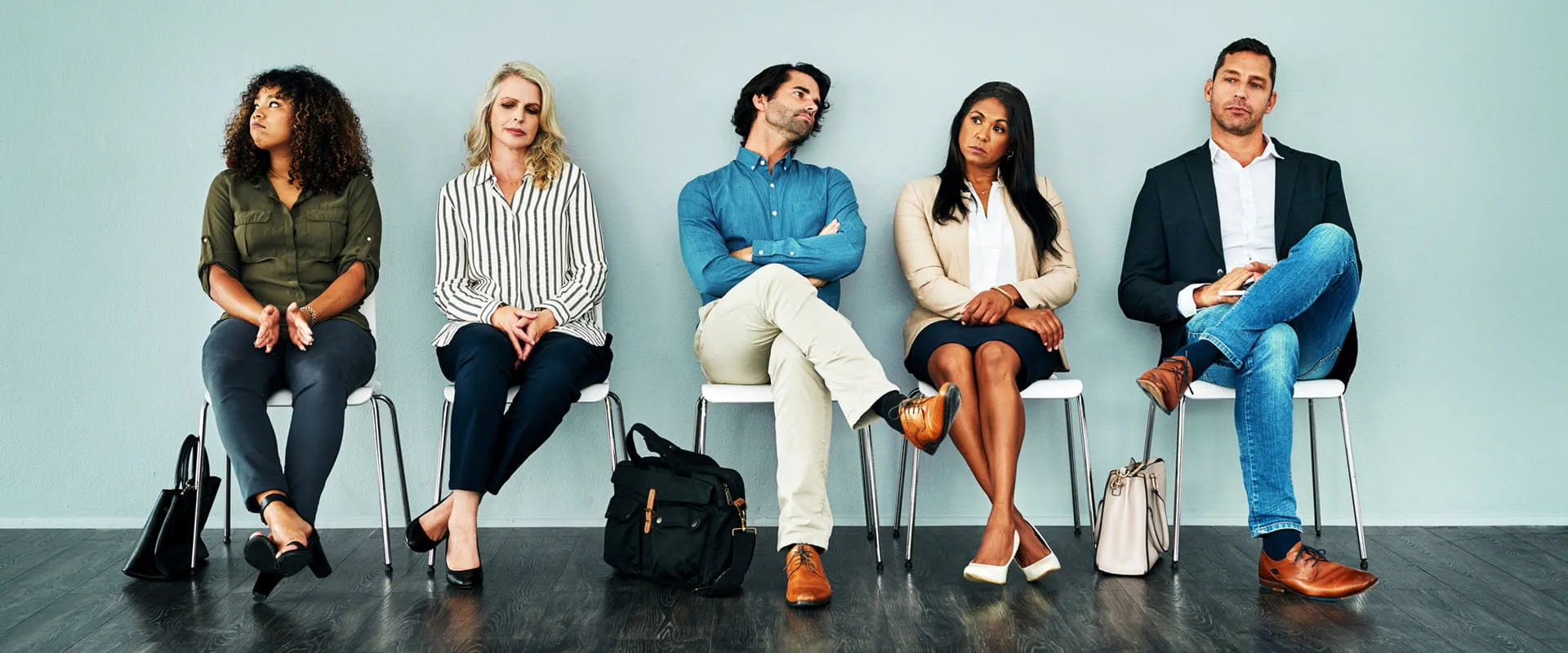 Five workers in business casual dress sit on white plastic chairs, looking bored or irritated Five workers in business casual dress sit on white plastic chairs, looking bored or irritated