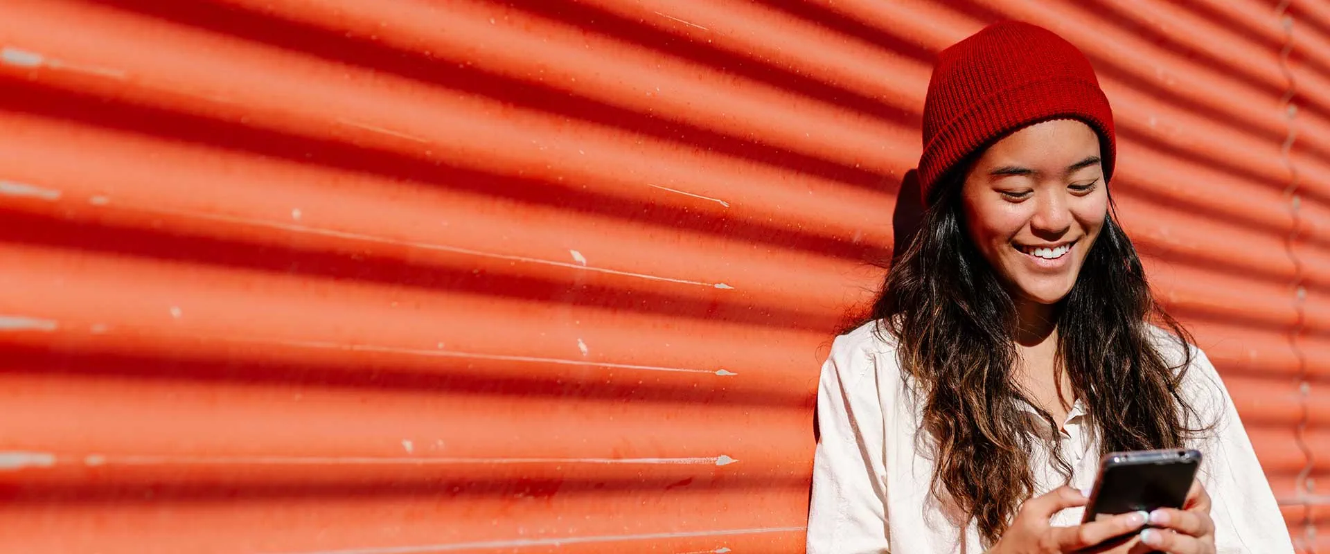 Woman in a red beanie using a smartphone against a bold red background Woman in a red beanie using a smartphone against a bold red background