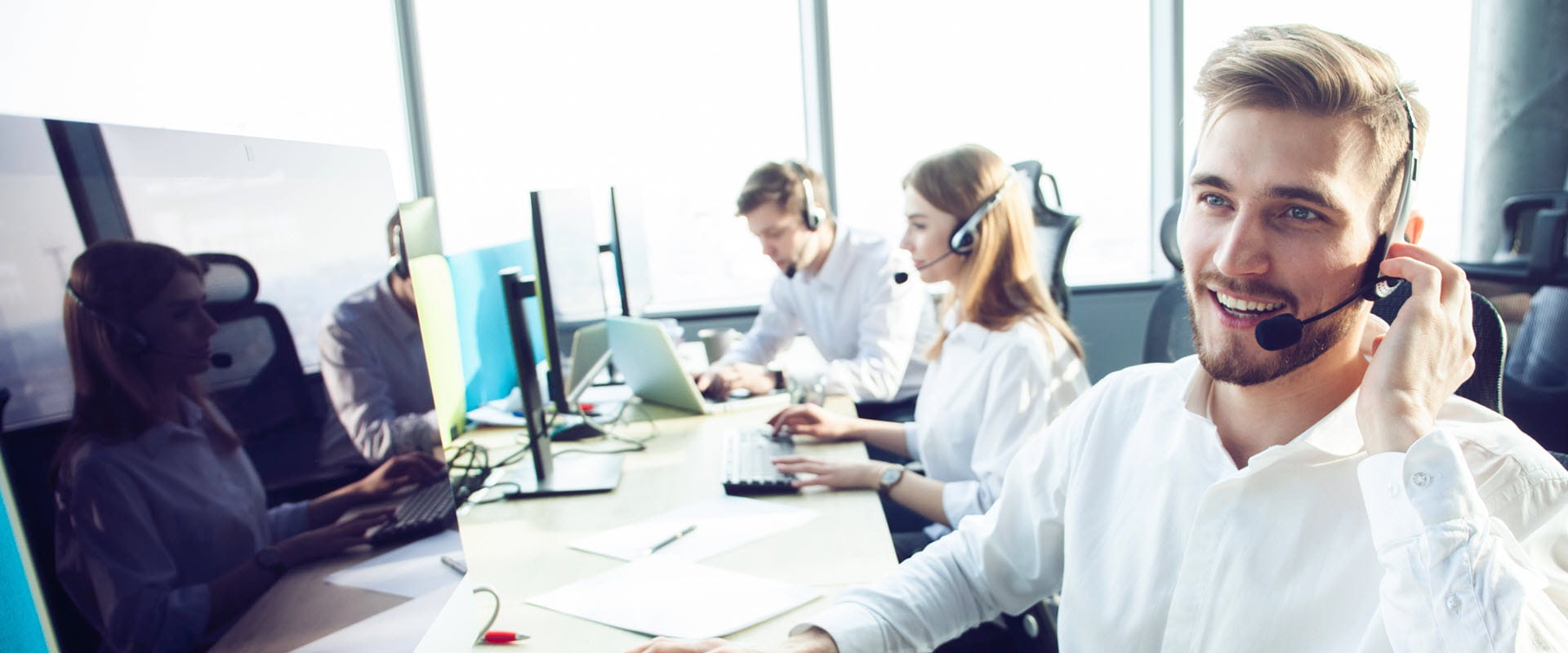 Customer support representatives working in a call center, wearing headsets and using computers.