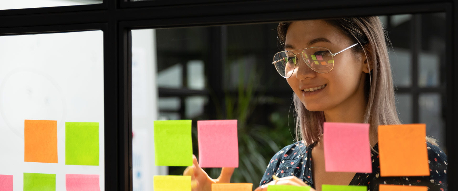 A professional organizing ideas with colorful sticky notes on a glass wall in a modern office.