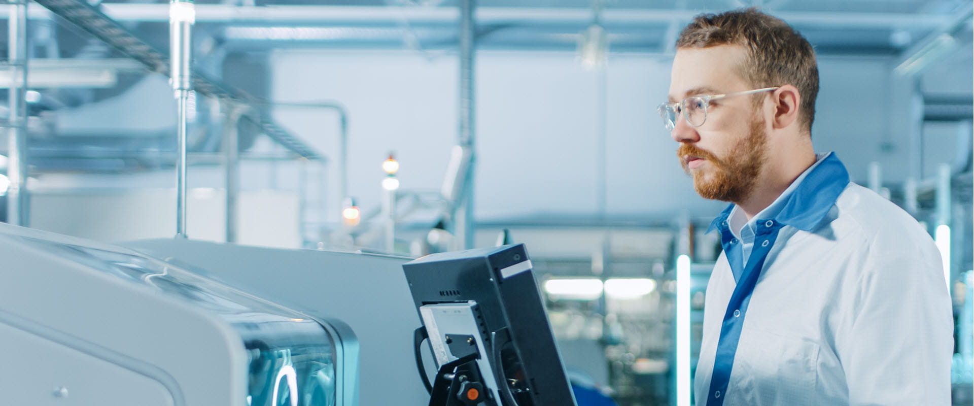 A technician wearing safety glasses and a lab coat operating advanced machinery in a laboratory.