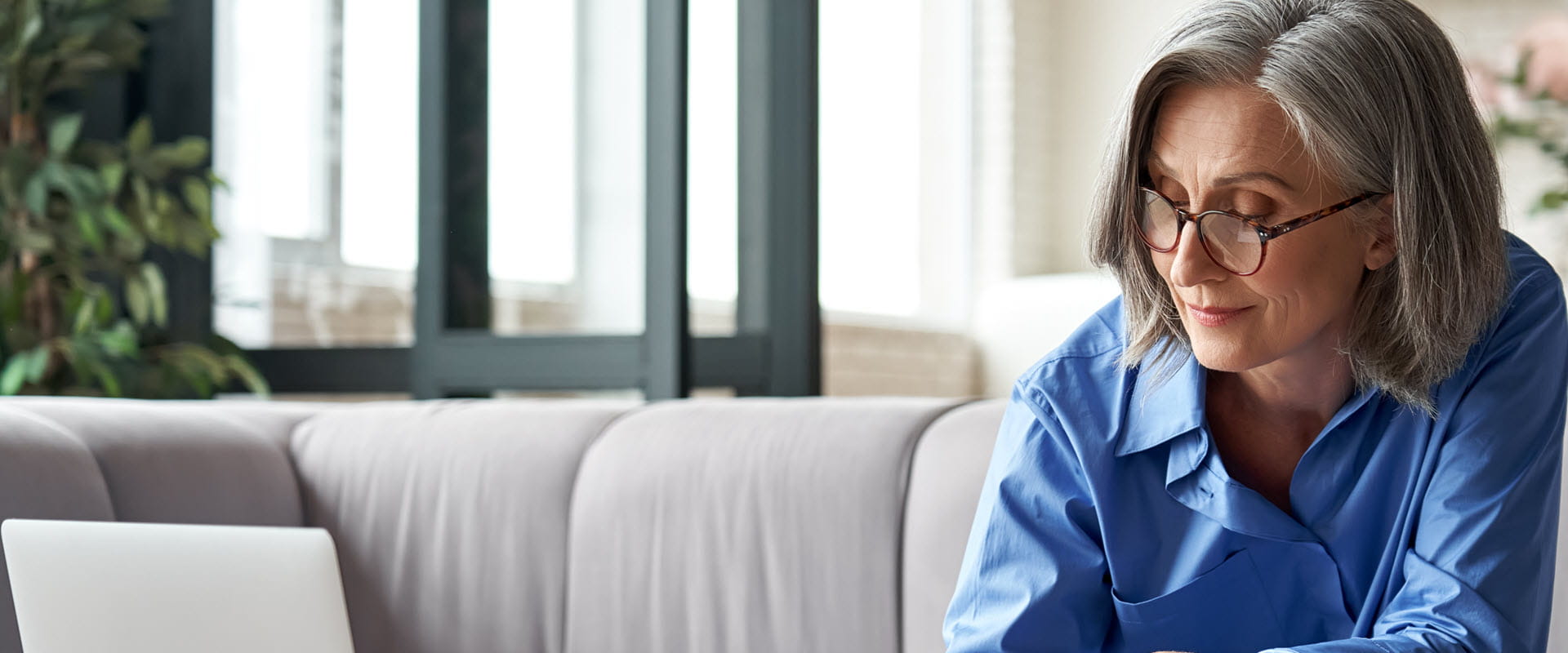 Woman sitting on couch with laptop on table, taking notes.