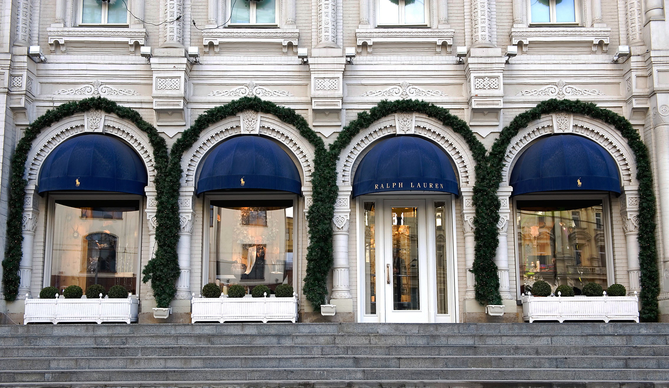 Ralph Lauren store front with blue awnings and decorative greenery, featuring a classic and sophisticated exterior.
